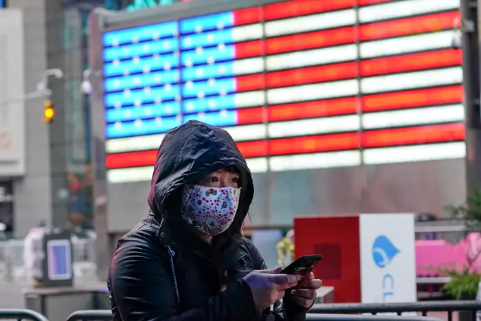 A woman wears a mask while in Times Square, passing by an NYPD stations that bears a neon image of the United States flag.